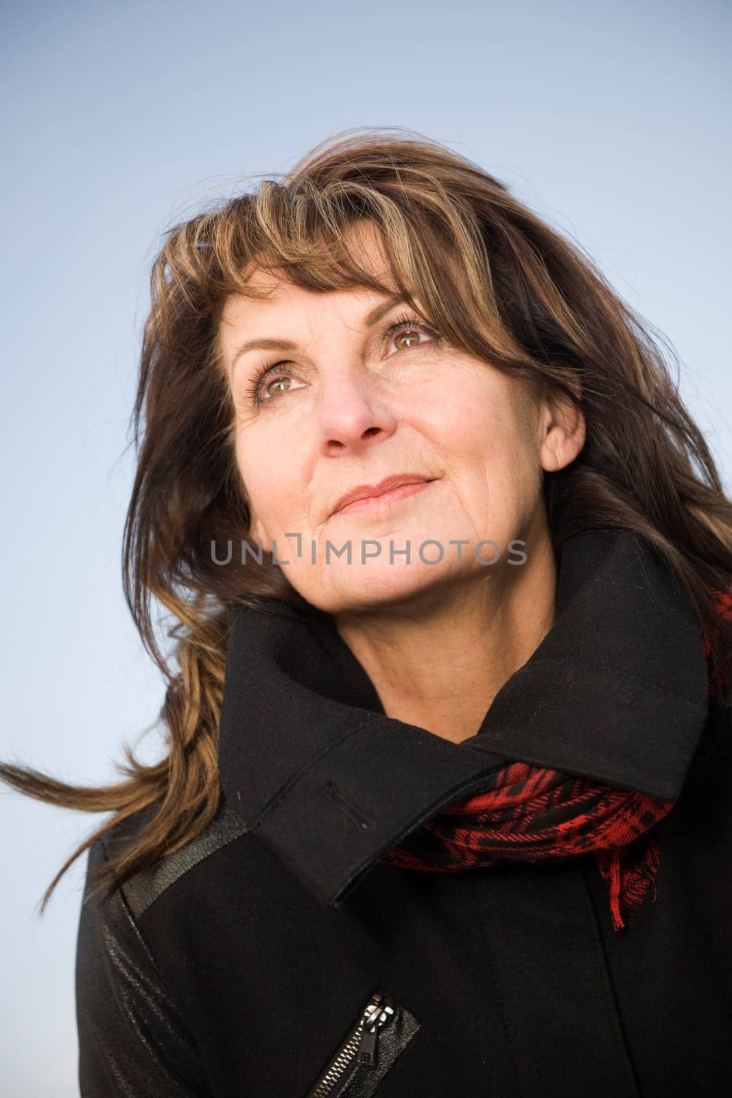 Head-port of a middle-aged woman in front of blue sky joyfully to the side and looking up