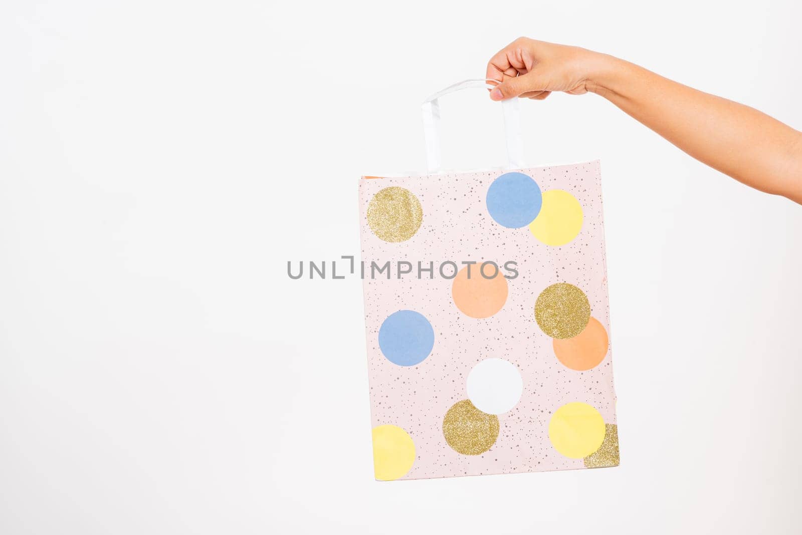 Closeup women hand holding a colorful pink shopping bag circular pattern, studio shot isolated on white background, female holds in hand white clear empty blank craft paper gift bag for purchases
