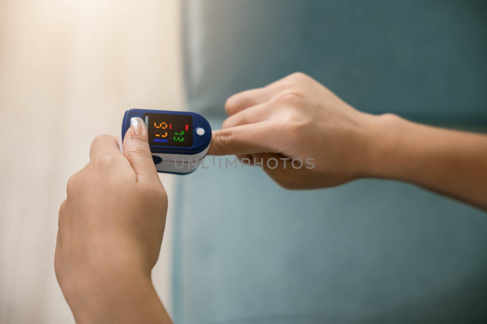 Young woman using pulse oximeter to monitor blood oxygen levels and pulse rate on finger under sofa in living room at home, Self healthcare with coronavirus pandemic, medical healthcare concept