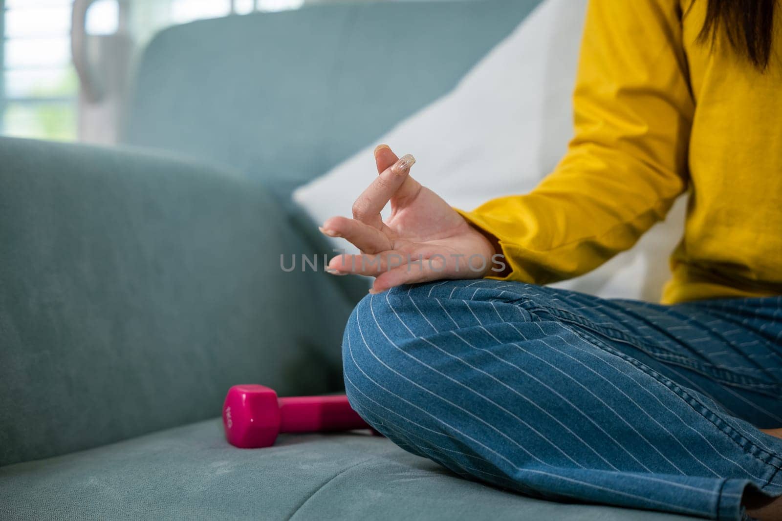 Young woman practise yoga and meditation in lotus position, mindfulness lifestyle, Asian female sits on sofa at home and chilling do yoga exercise with couch lotus pose eyes closed, healthy care