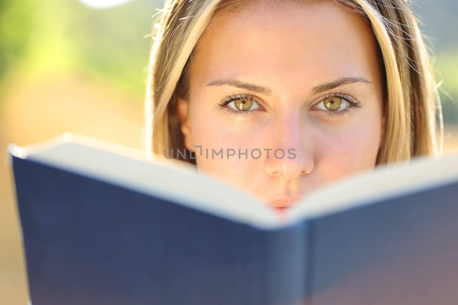 Front view of a beautiful woman reading a book looking at you with amazing eyes