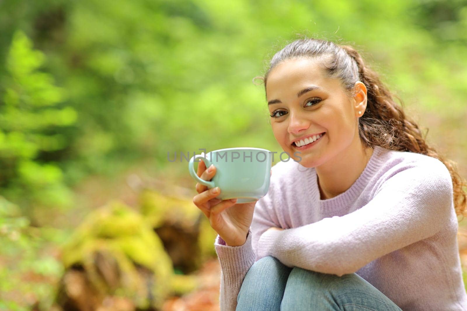 Happy woman sitting in nature holding coffee cup posing looking at camera