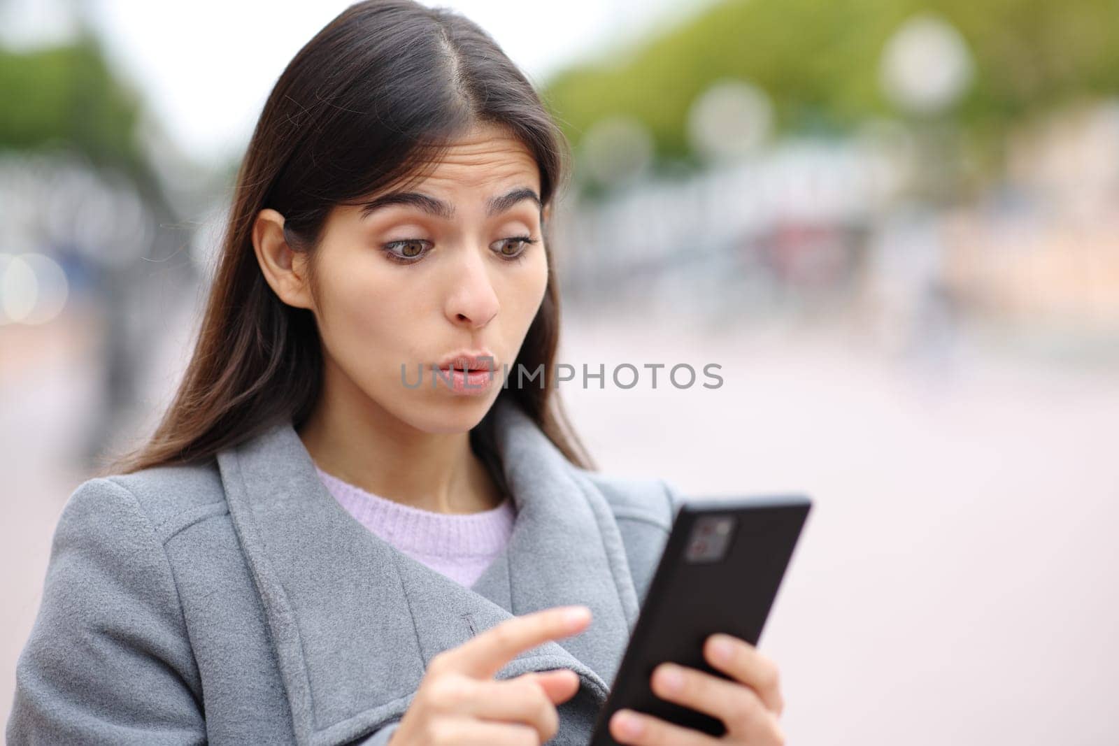 Upset woman saying oops watching phone content in the street in winter