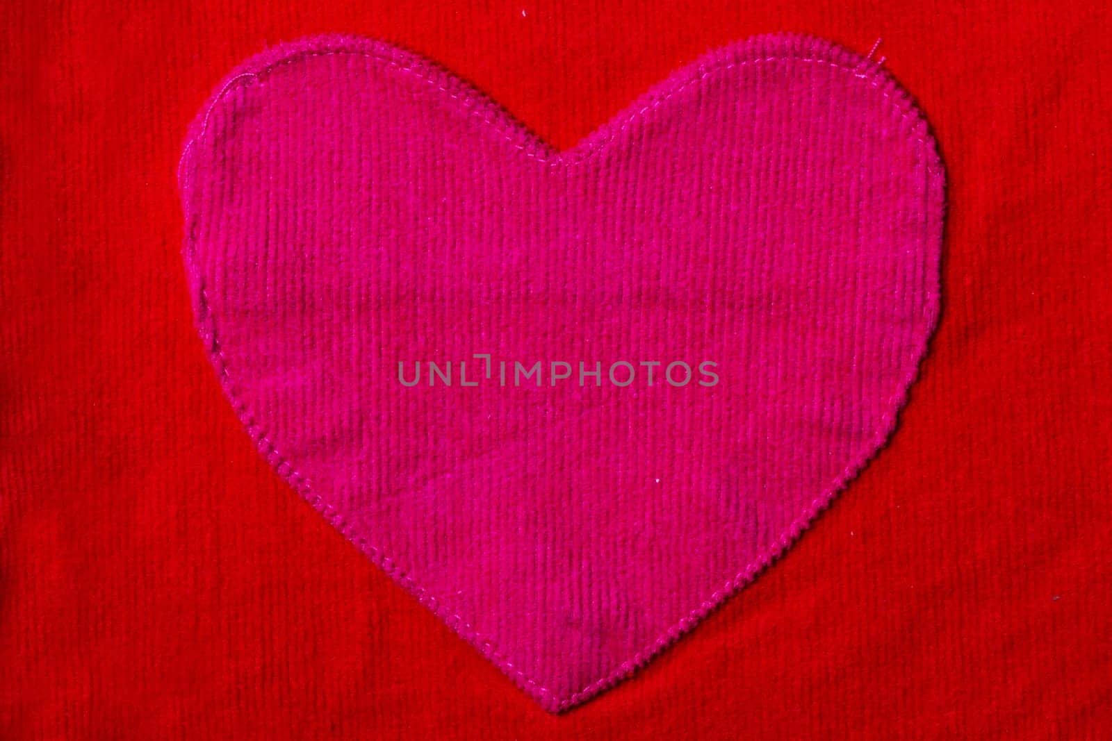 Closeup of large pink heart on red fabric background texture. Valentine's or mother‘s day concept. Copy space.