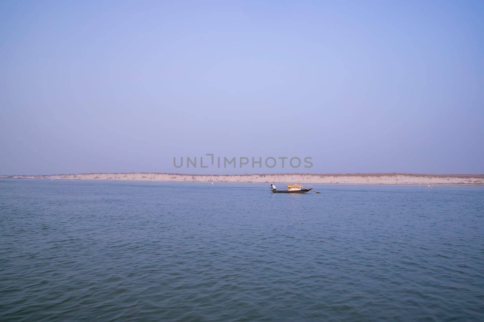 landscape view of Padma river on a fishing boat with a sand island under the blue sky