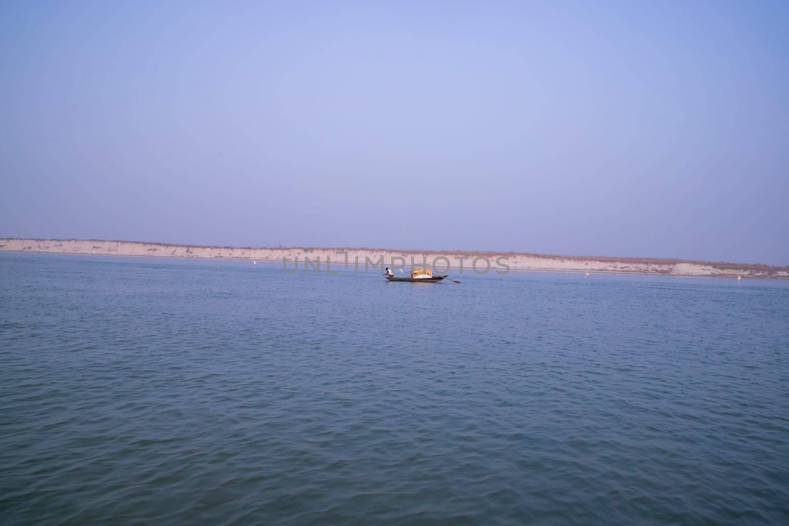 landscape view of Padma river on a fishing boat with a sand island under the blue sky