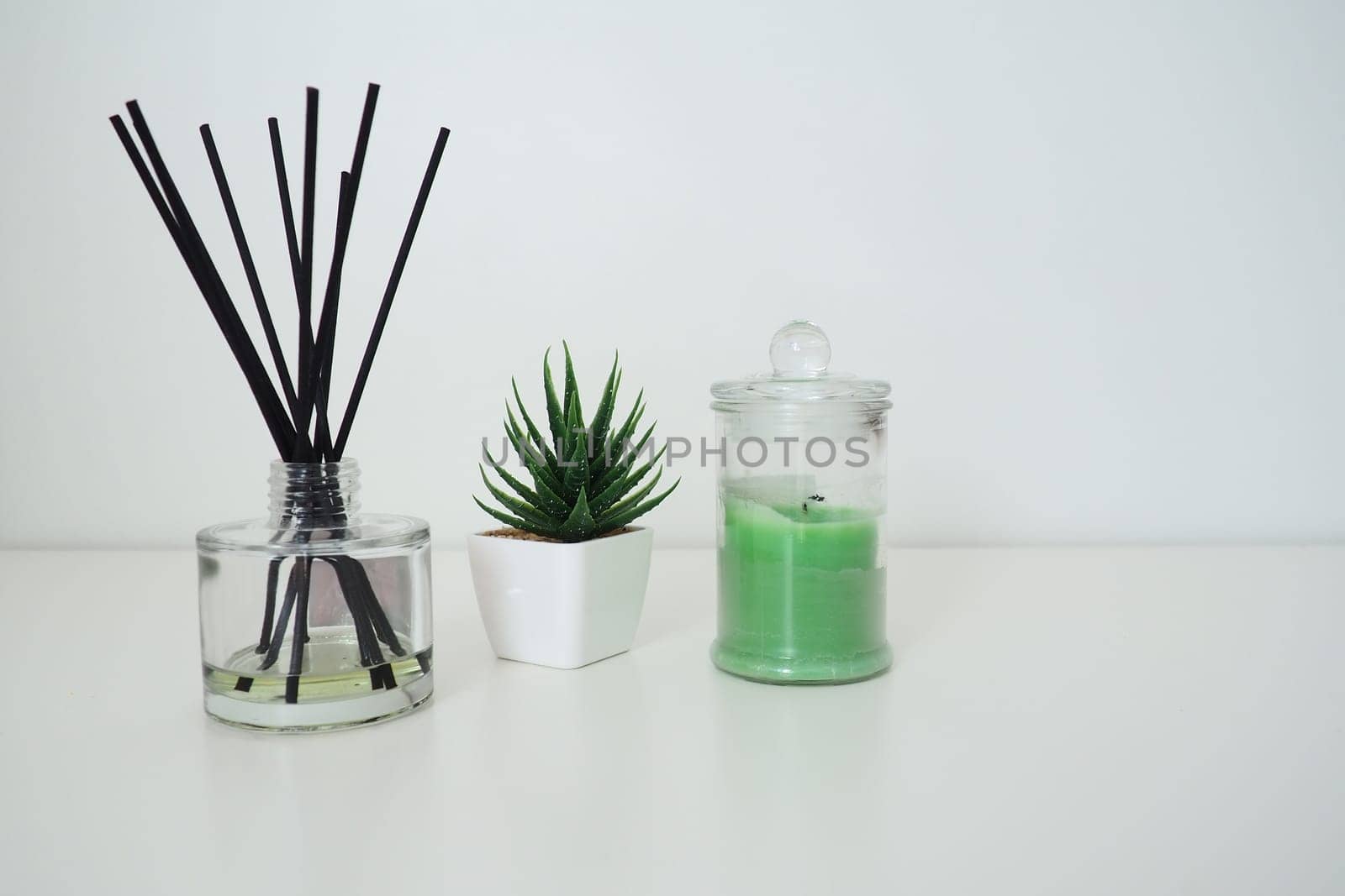 Incense sticks in a glass cubic vessel with essential oils. Interior decor. White background. Sansevier or aloe plant in a pot. Copy space. Wax candle in a stylish glass flask with a lid.