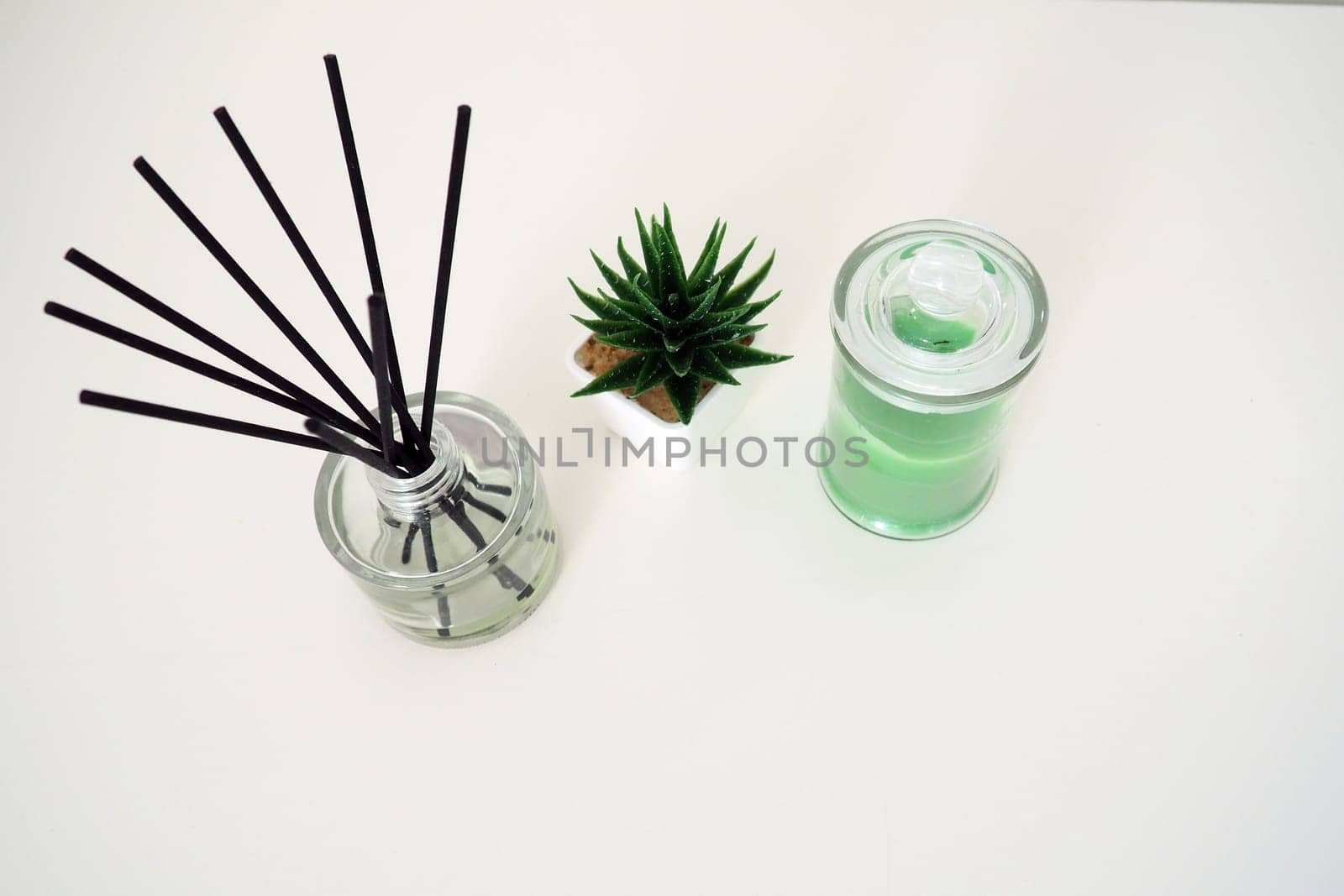 Incense sticks in a glass cubic vessel with essential oils. Interior decor. White background. Sansevier or aloe plant in a pot. Copy space. Wax candle in a stylish glass flask with a lid.