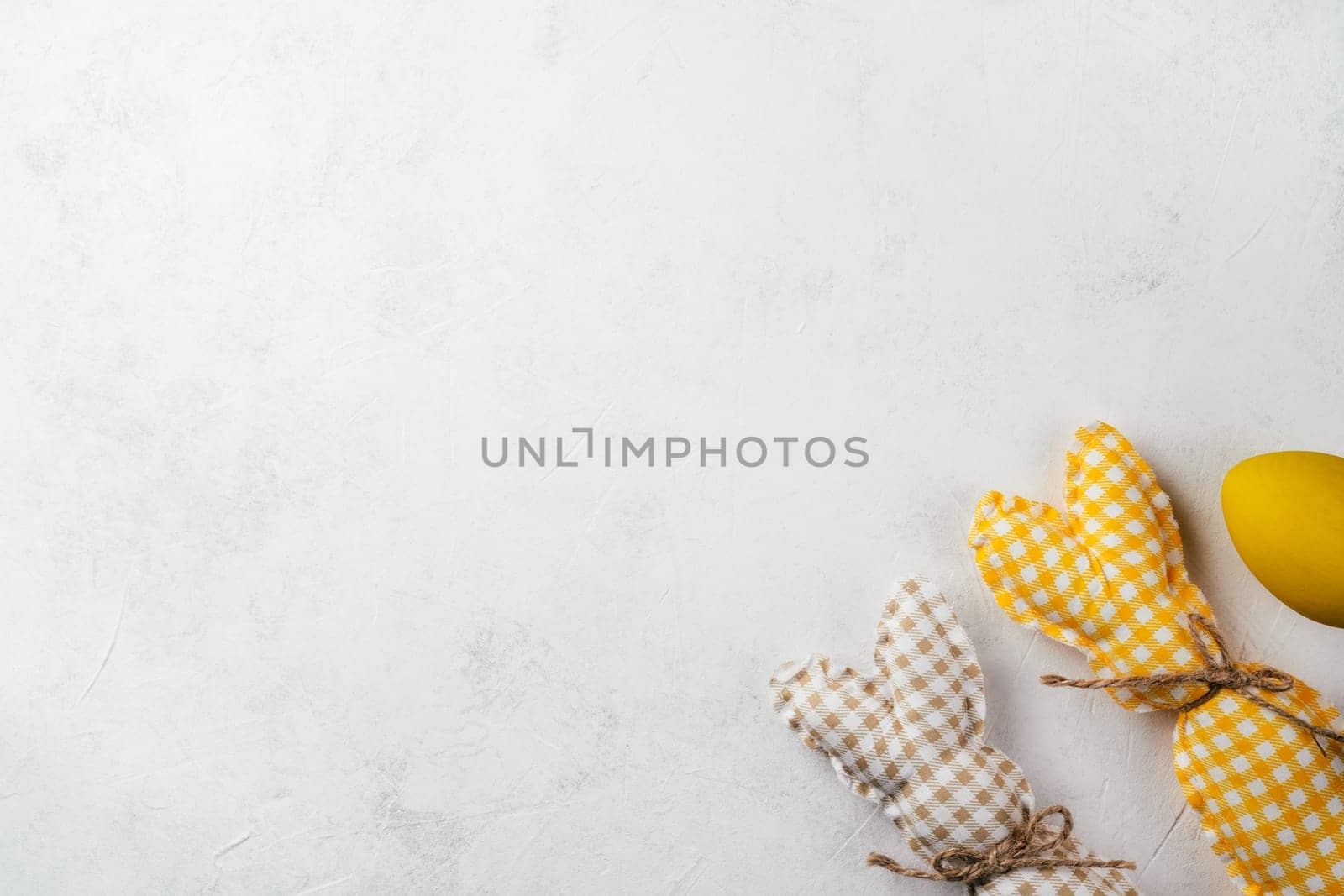 Easter postcard for celebration holiday, two handmade square brown, white and yellow colored bunnies with strings-scarfs on white gray paper background, yellow chicken egg. Copy space, place for text.