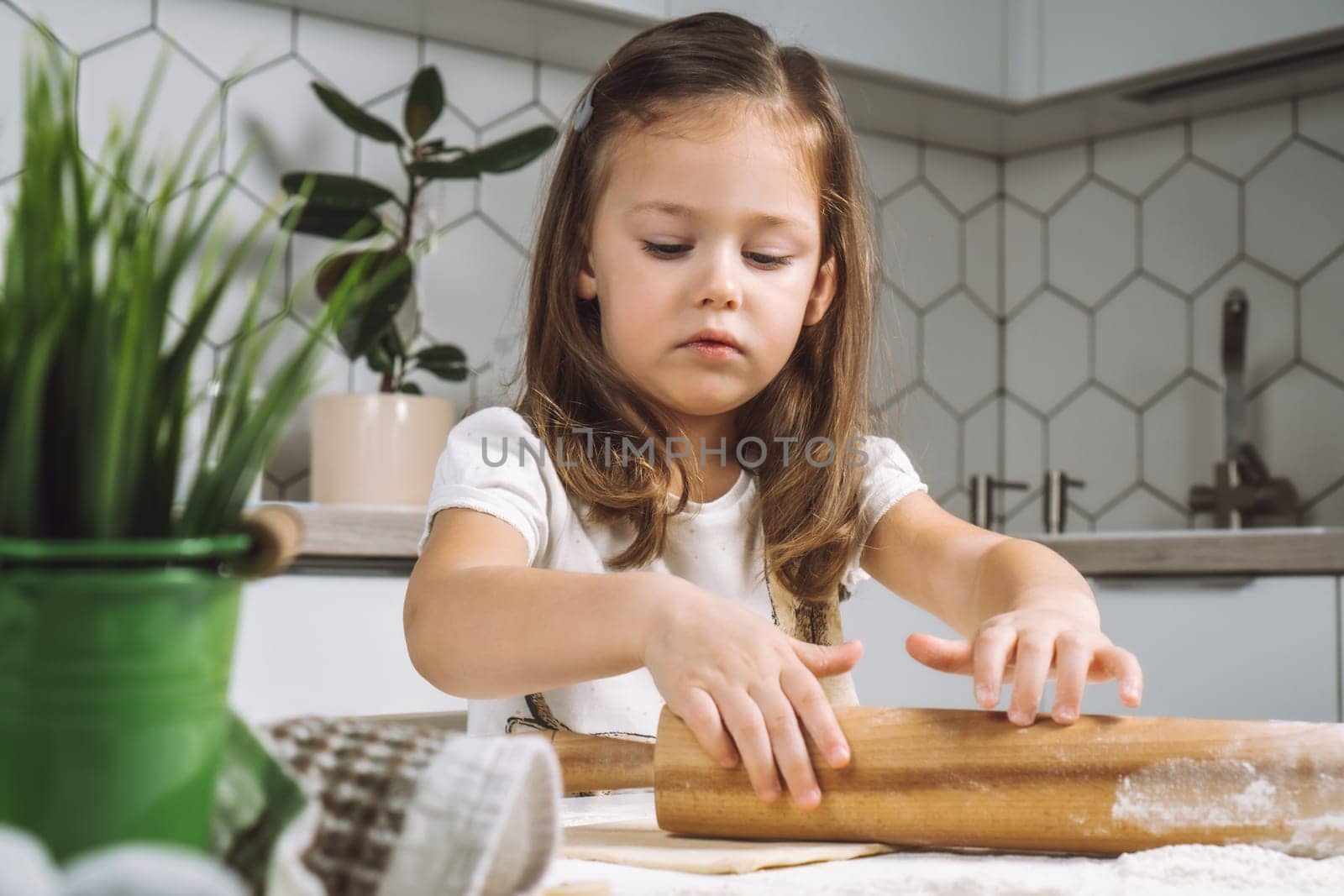 Portrait of little serious girl, helping, learning rolling dough, making shape easter cookies. Sculpt flour biscuit. Preparing holding rolling pin flour. Plant child. Kitchen indoor utensil. Light day