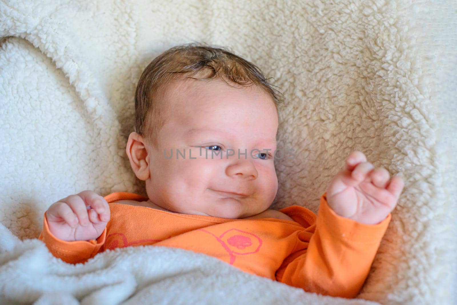 Kid in orange clothes raised his hand up while lying on a white blanket