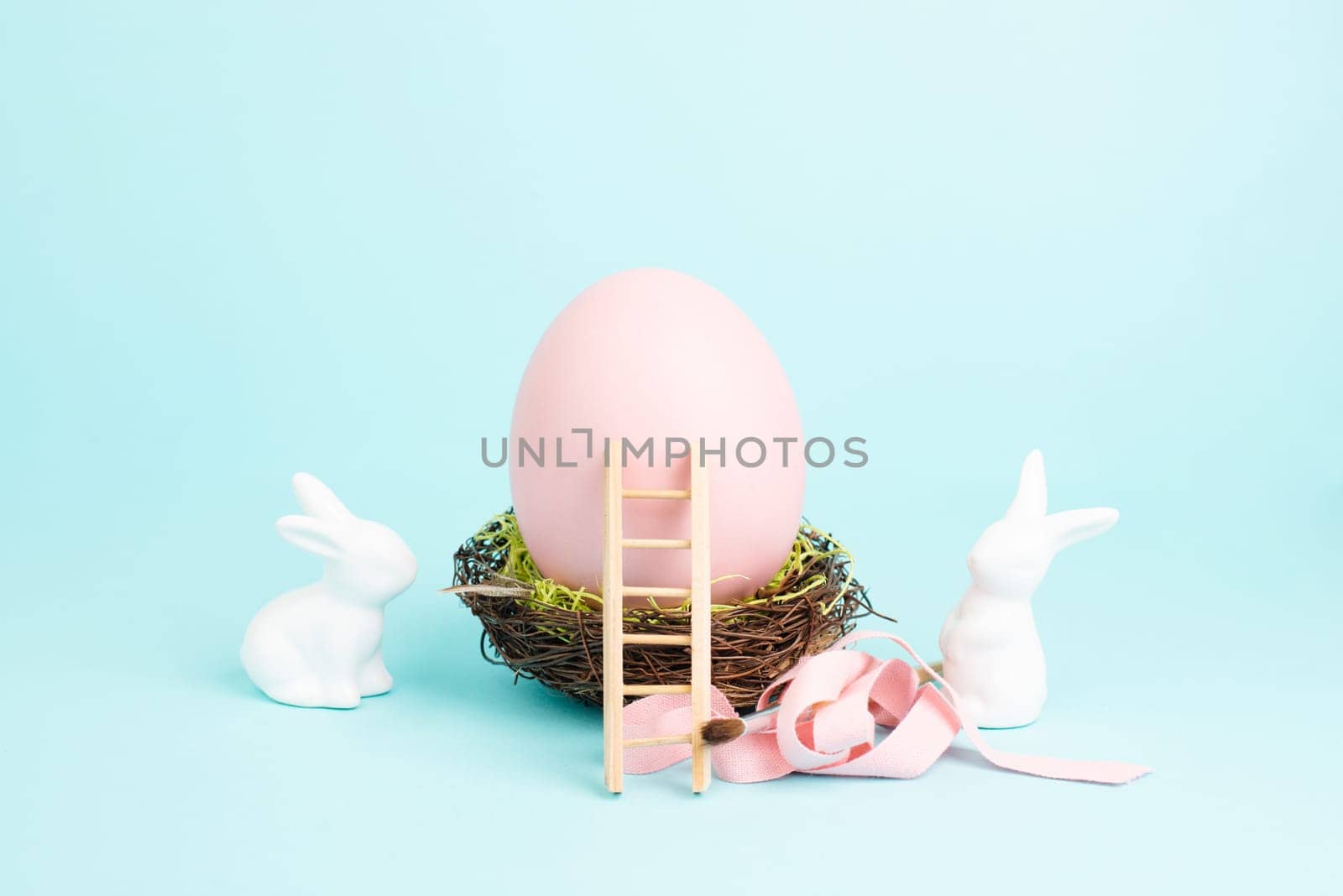 Easter bunny or rabbit sitting next to a huge pink colored egg in a birds nest, gift ribbon and ladder, spring holiday