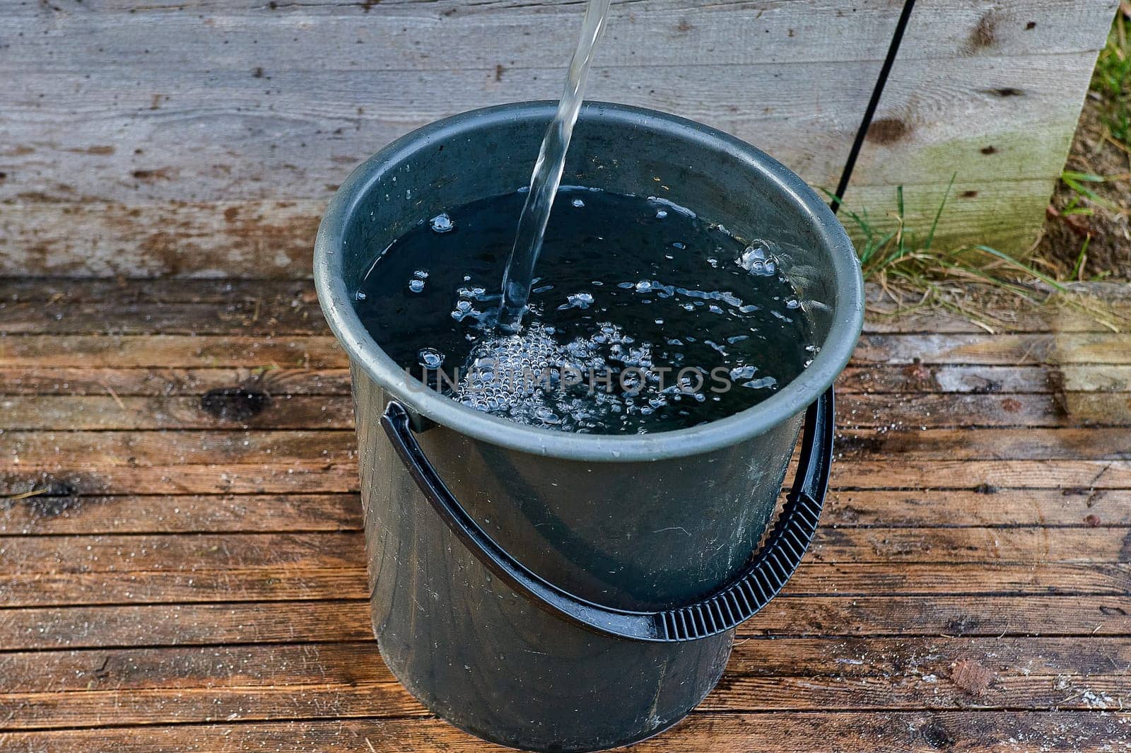 a black plastic bucket is filled with water from the pump. High quality photo