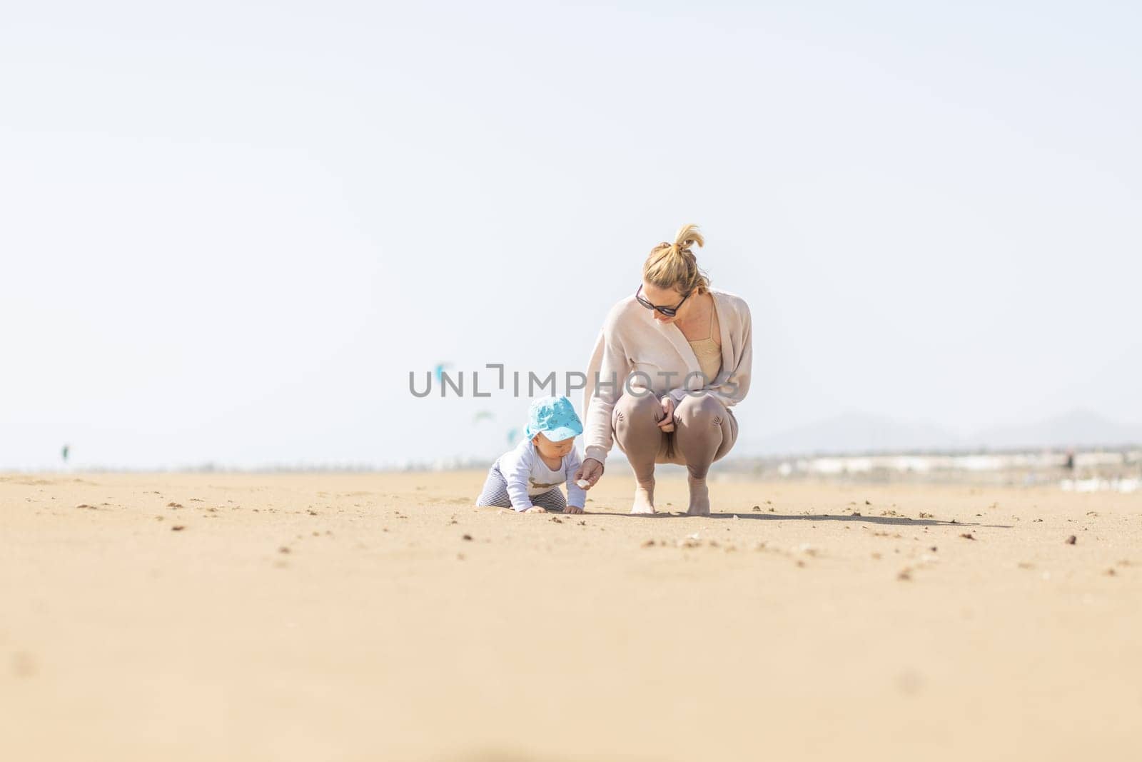 Mother playing his infant baby boy son on sandy beach enjoying summer vacationson on Lanzarote island, Spain. Family travel and vacations concept.