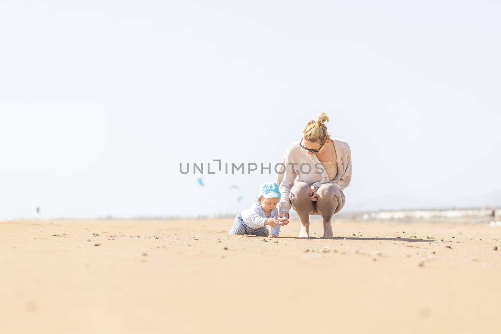 Mother playing his infant baby boy son on sandy beach enjoying summer vacationson on Lanzarote island, Spain. Family travel and vacations concept