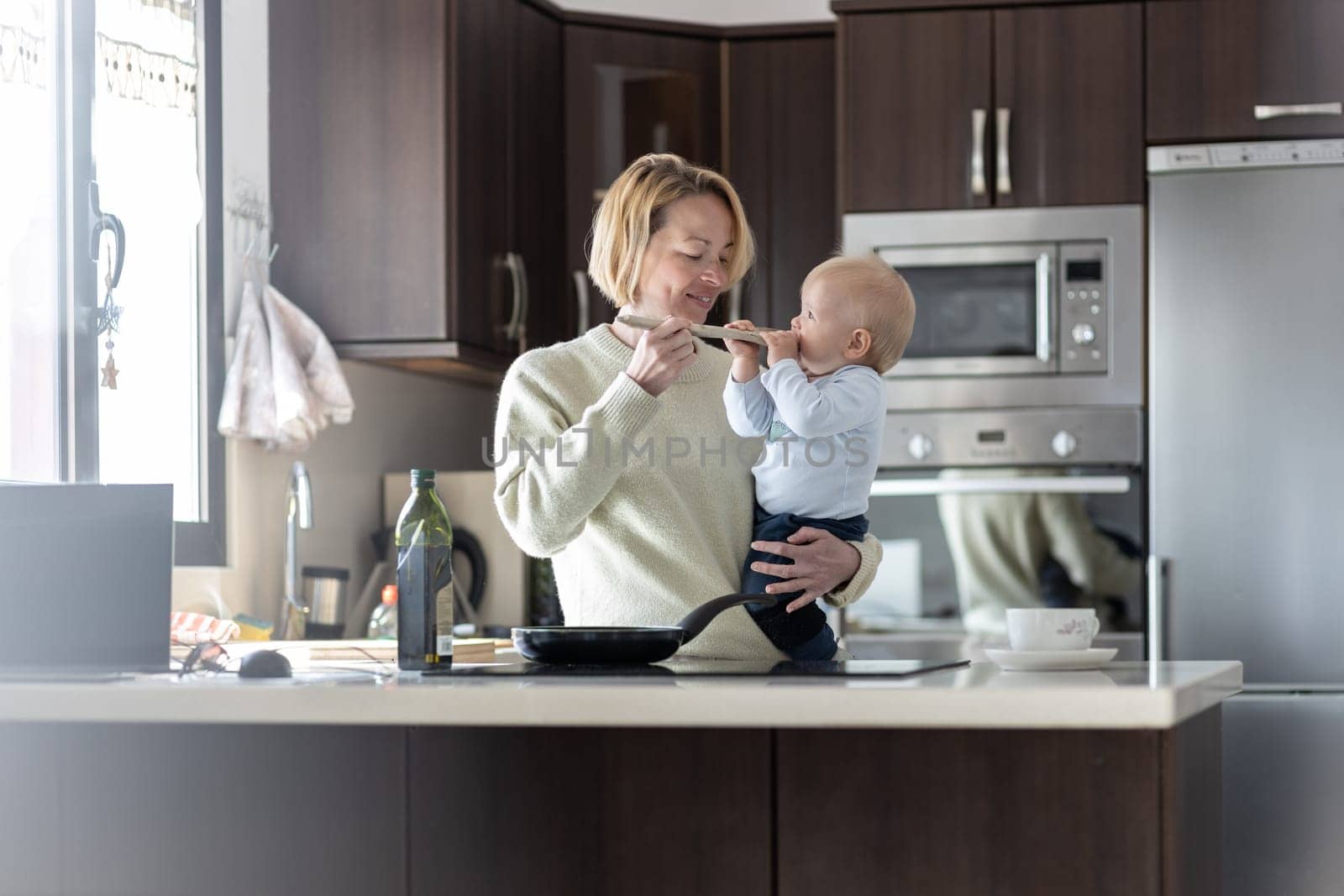 Happy mother and little infant baby boy cooking and tasting healthy dinner in domestic kitchen. Family, lifestyle, domestic life, food, healthy eating and people concept