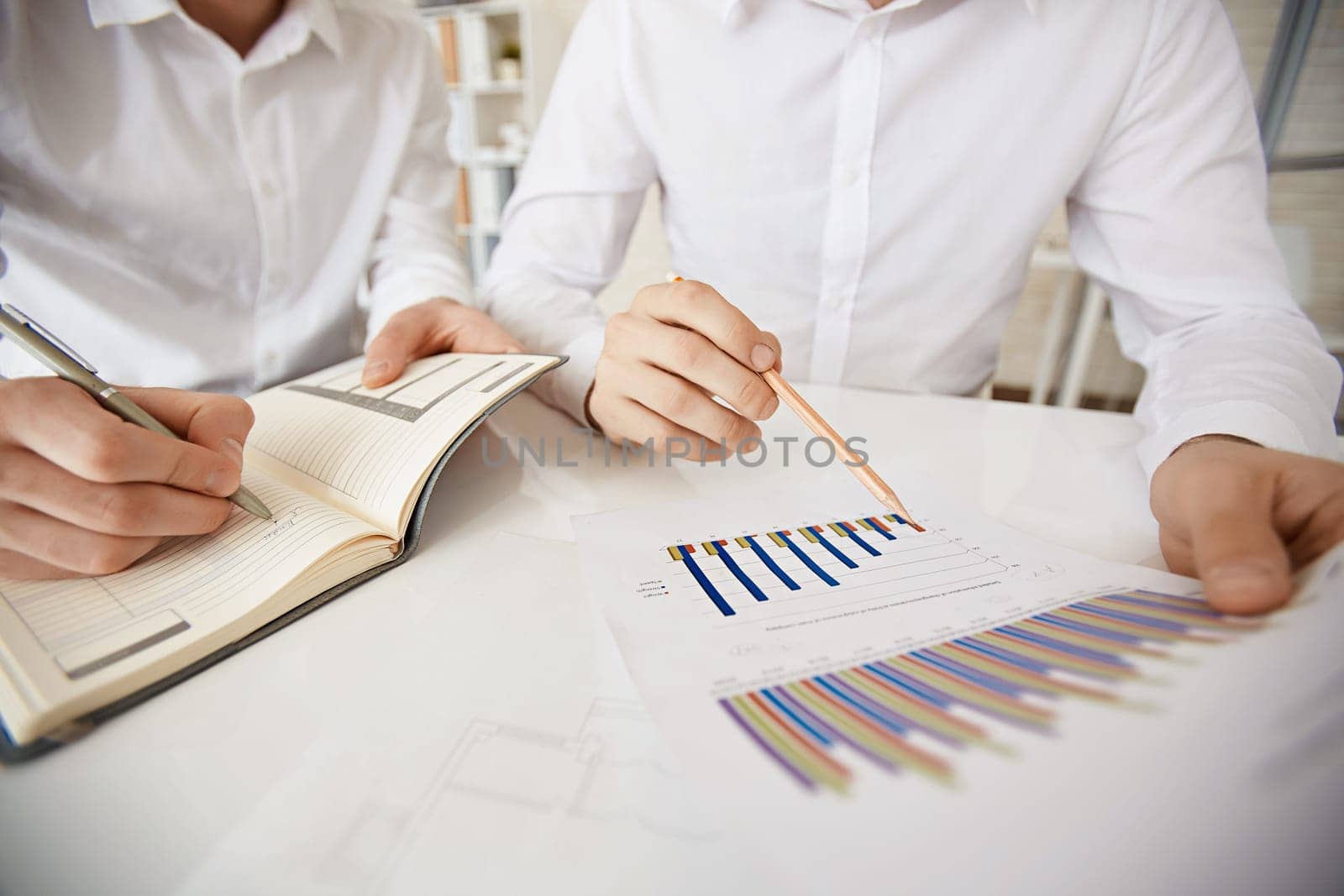 Hand of businessman with pencil pointing at data in document while his colleague making notes