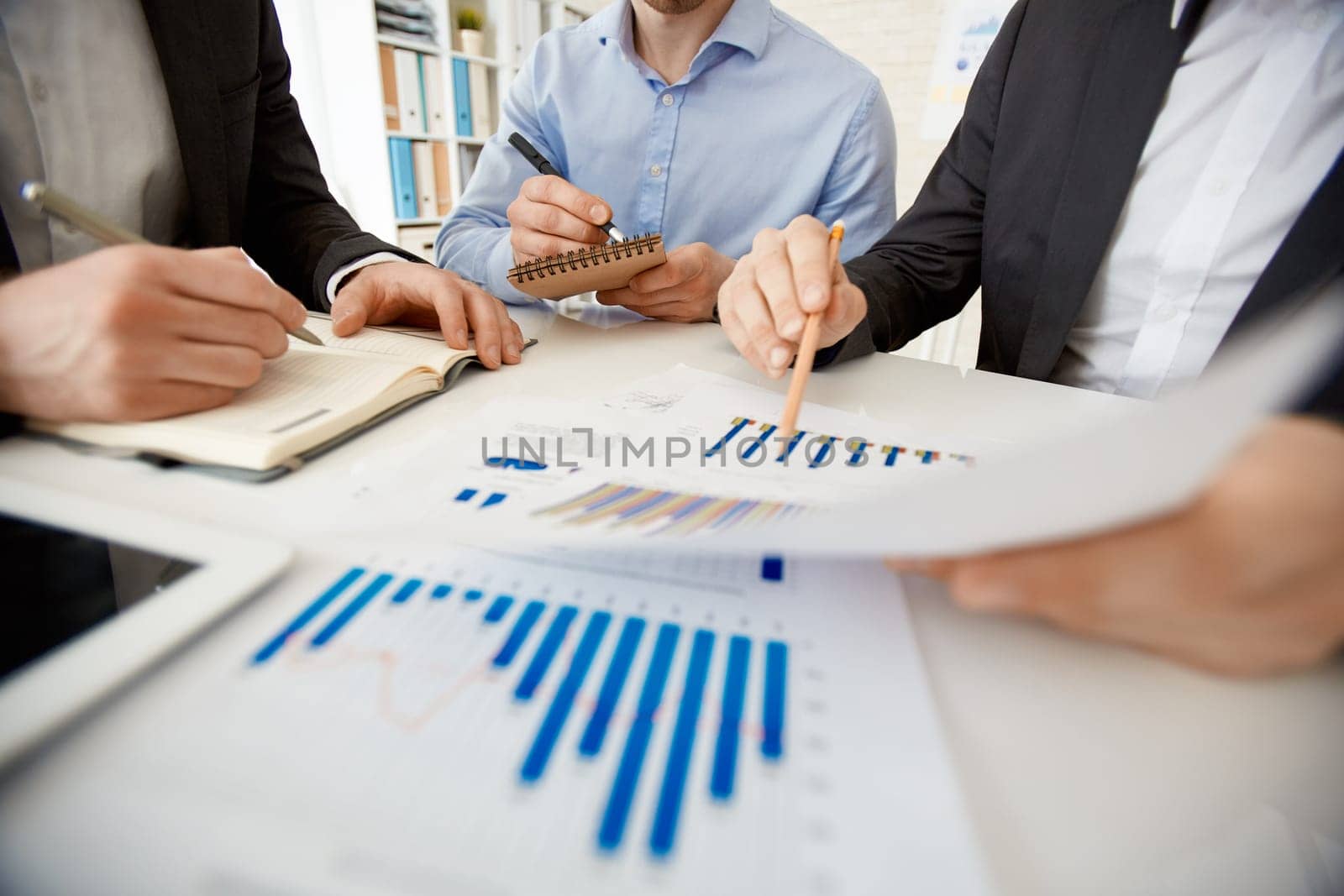 Businessman pointing at paper with chart while explaining it to colleagues at workplace