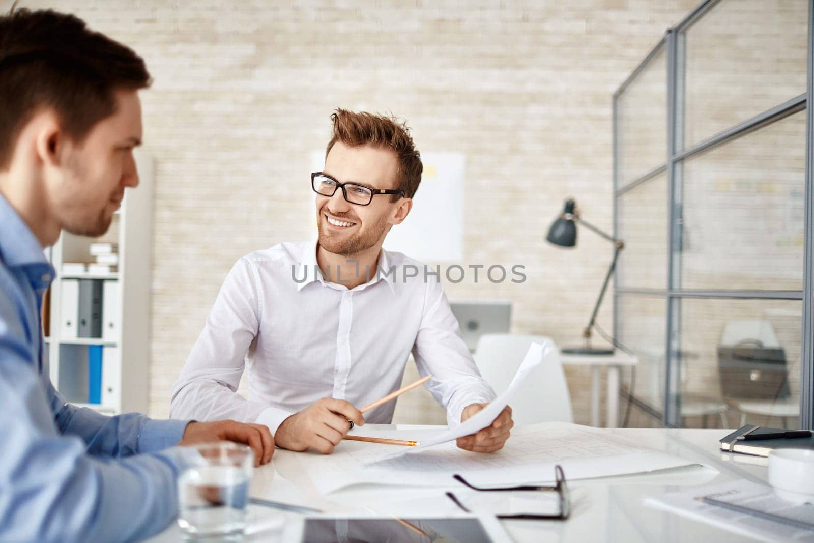 Young businessman looking at co-worker during explanation of document