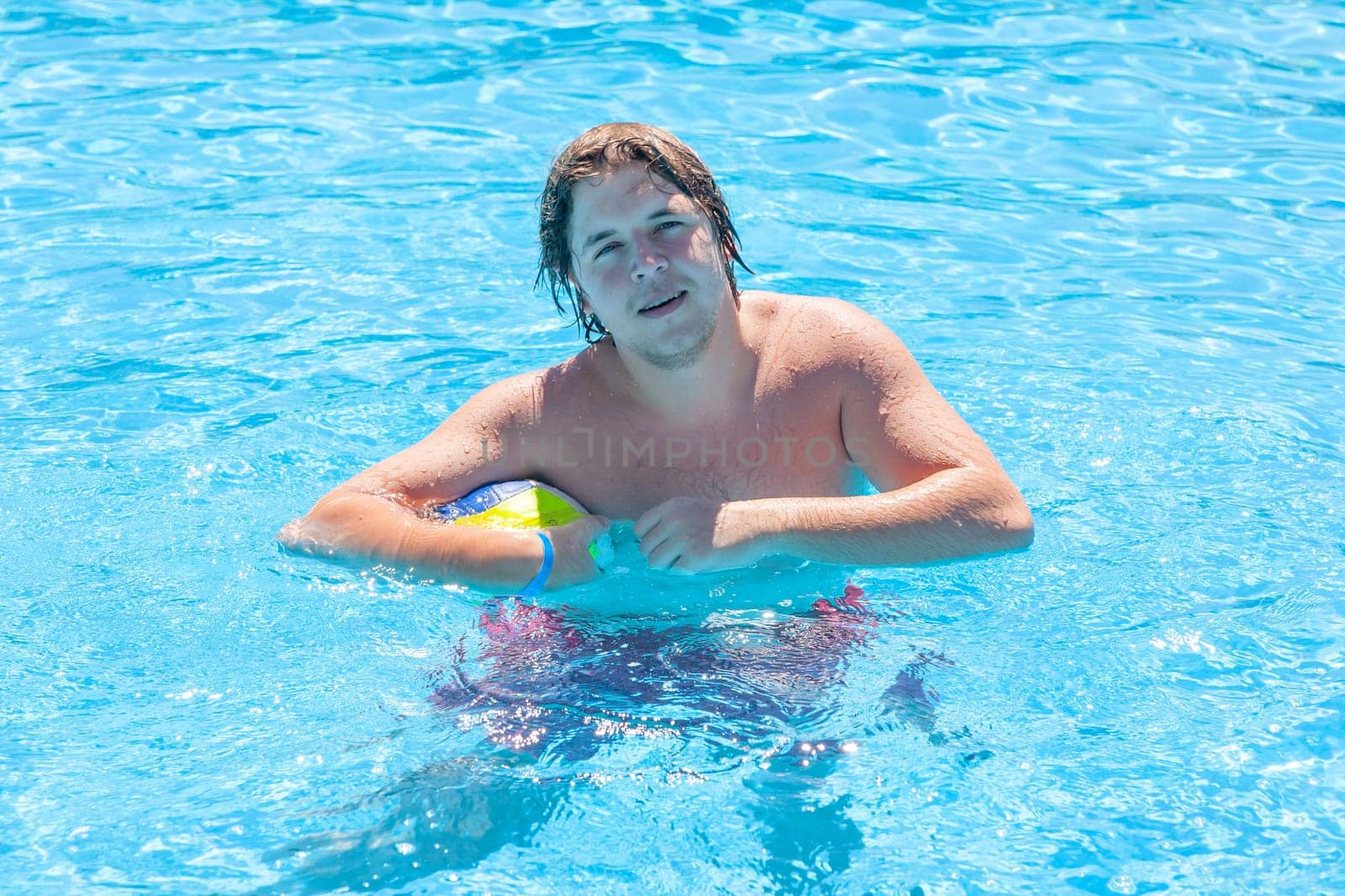 Happy man with water ball playing in a swimming pool in summer