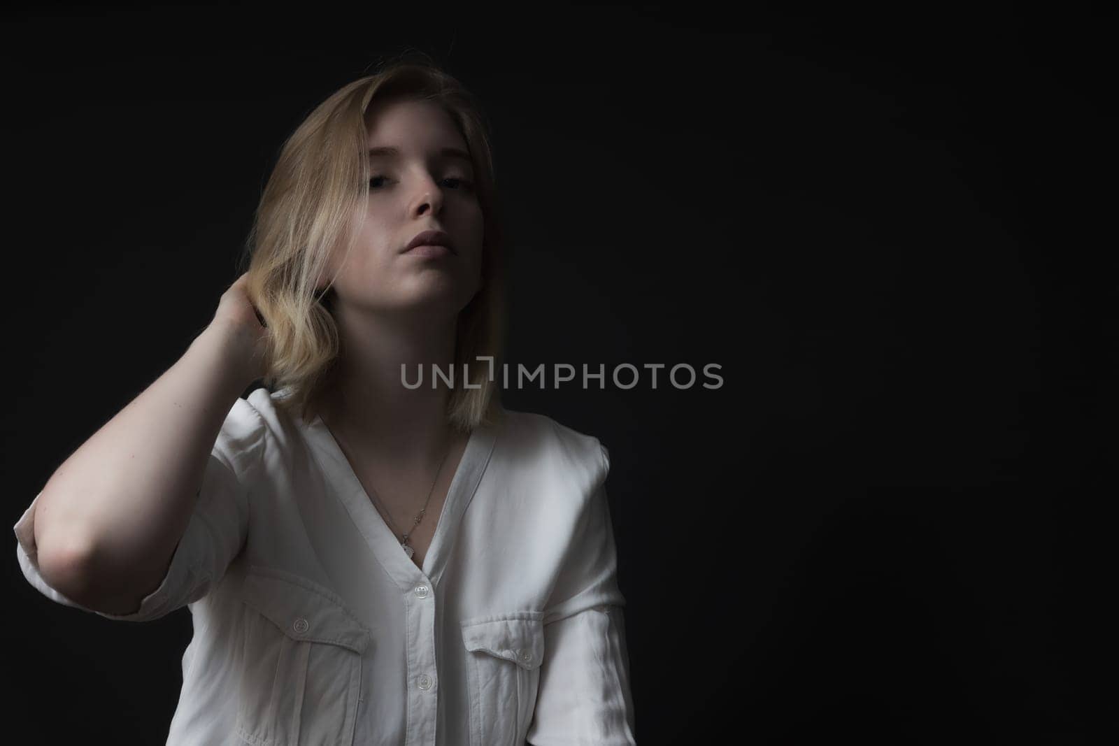Serious blondes girl weared in white shirt is posing on black background.