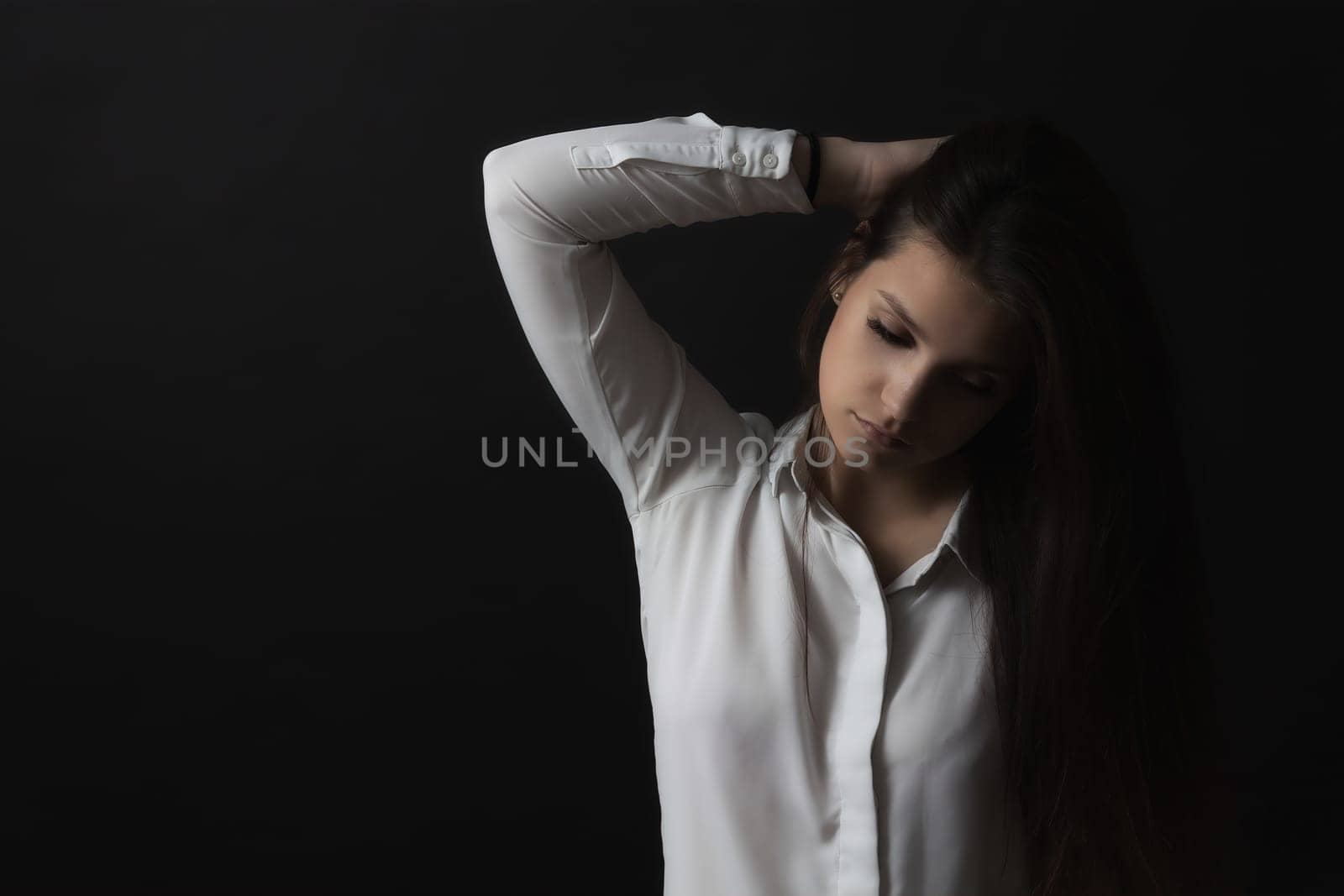 Low key portrait of long haired sad young woman weared in white shirt. Horizontally.