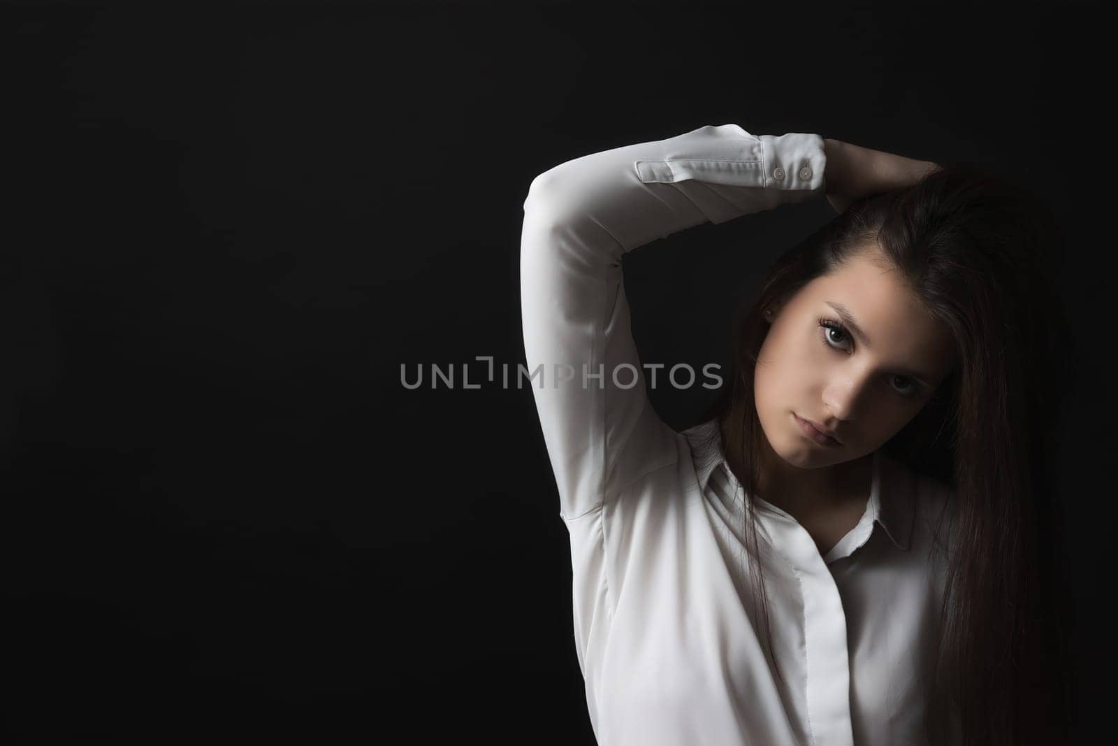 Beautiful sad girl weared in white shirt is posing on black background.