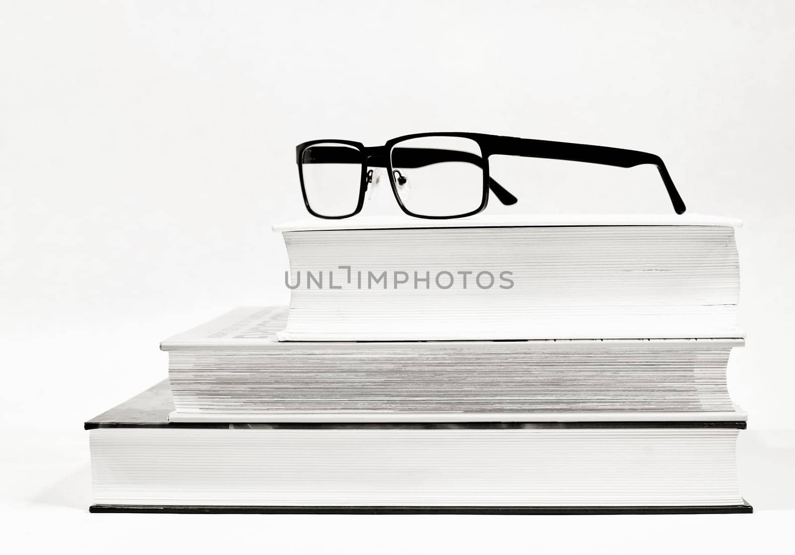 Three thick books and glasses as a visual aid as black and white picture