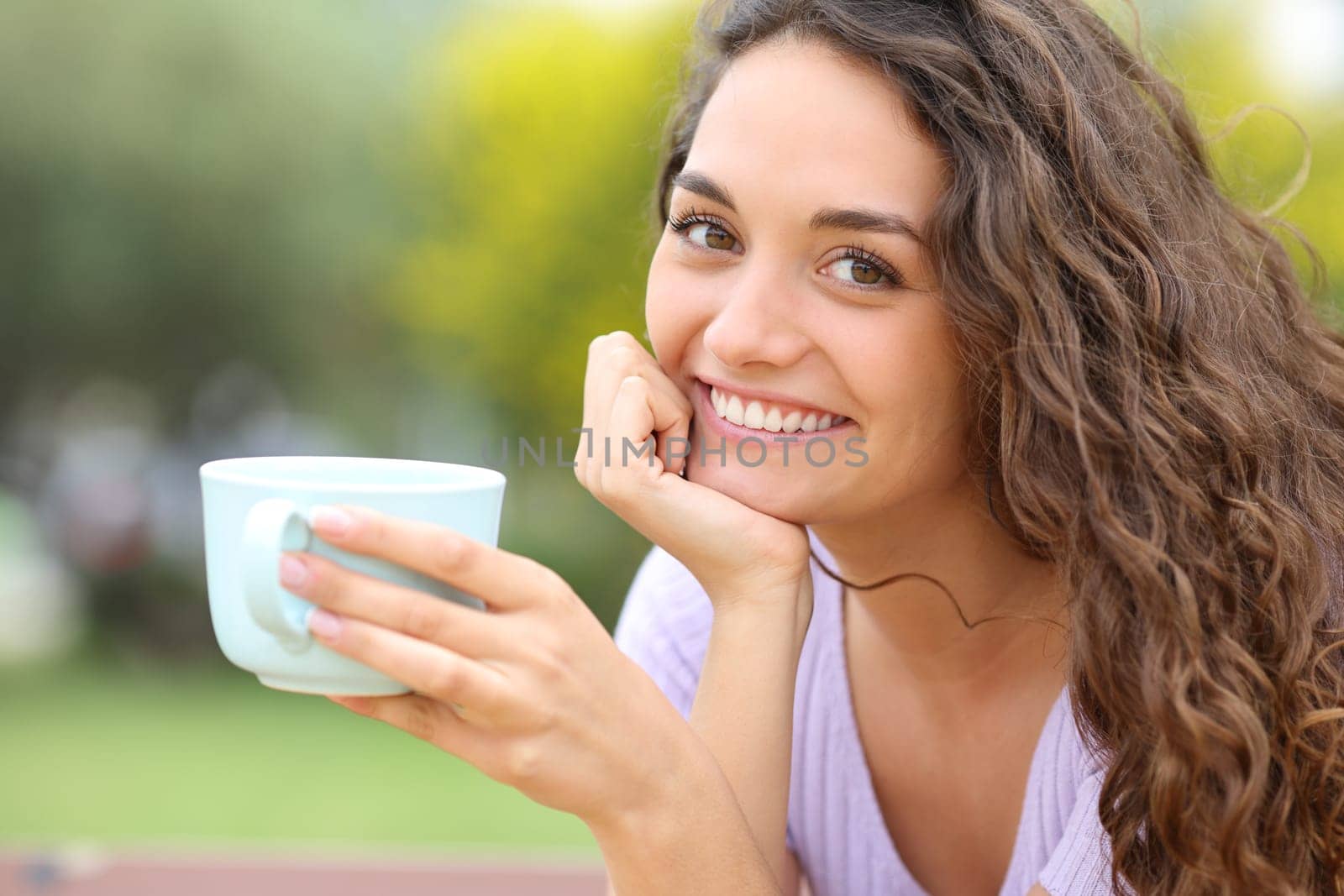 Happy woman holding coffee cup posing in a park