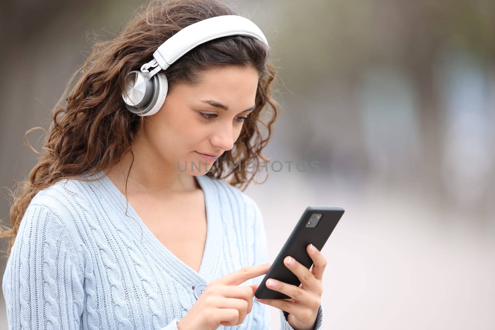 Woman wearing headphones checks phone outdoors in the street