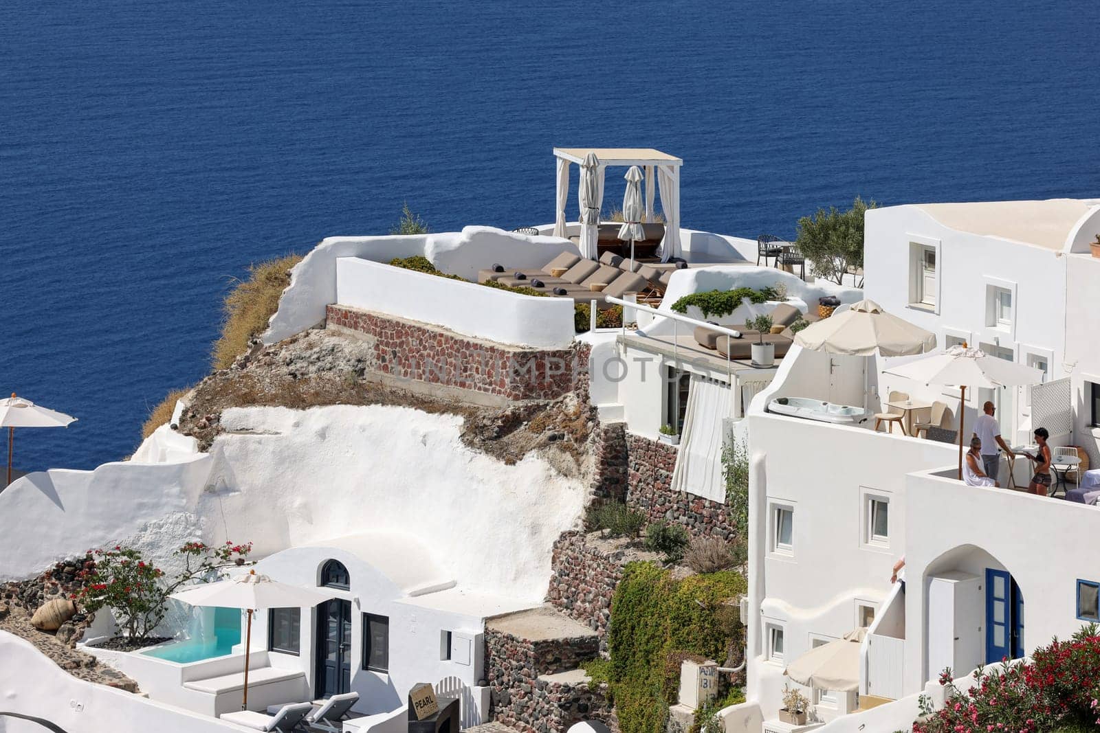 Oia, Santorini, Greece - July 3, 2021: Whitewashed houses with terraces and pools and a beautiful view in Oia on Santorini island, Greece