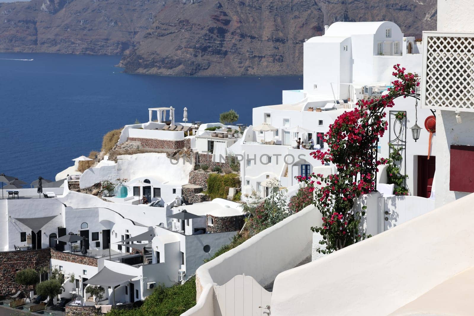 Oia, Santorini, Greece - July 3, 2021: Whitewashed houses with terraces and pools and a beautiful view in Oia on Santorini island, Greece