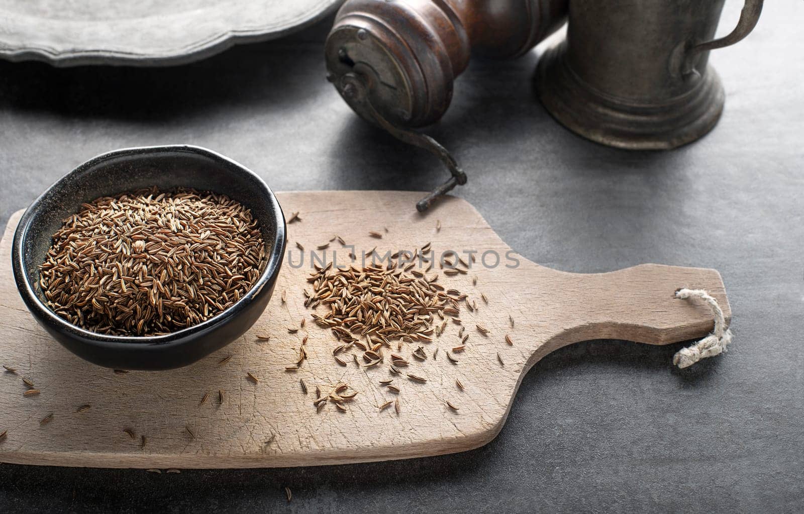 Pile of Cumin seeds and cumin seeds in bowl on grey background close up