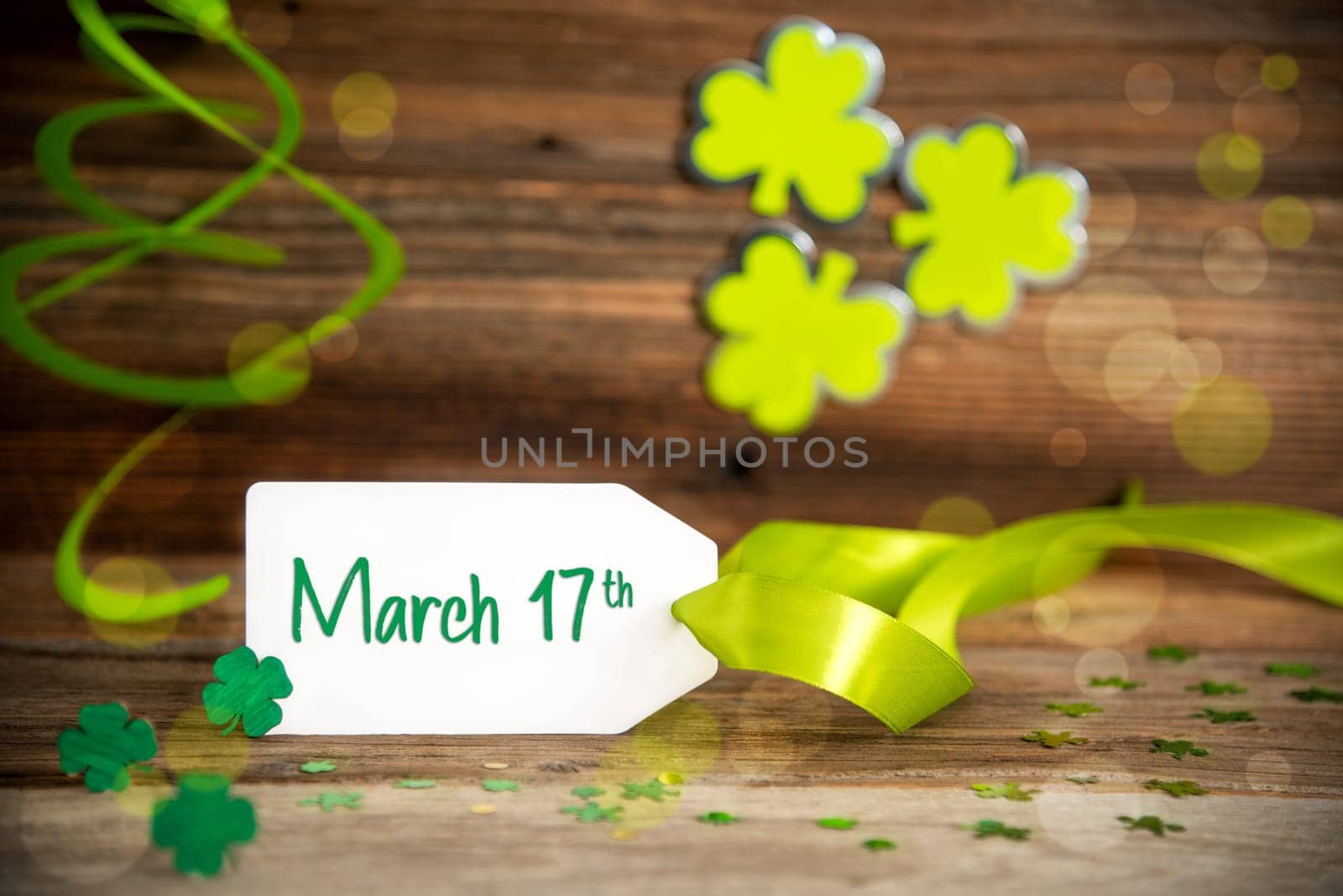 White Label With English Text March 17th. Saint Patrick's Day Decoration With Green Shamrock And Clover. Wooden Vintage Background With Festive Ribbon.