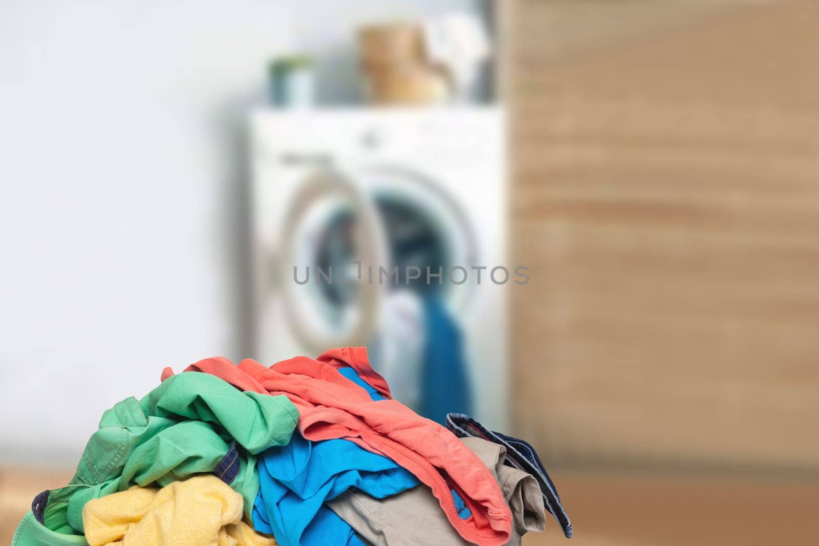 Stack or pile of colorful dirty clothes on table ready for the laundry in front of abstract blurred bath background with copy space. For your product display montage.