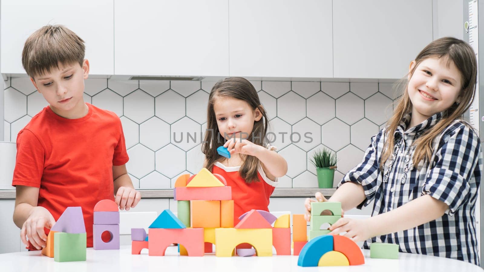 Happy school friends play toy constructor on kitchen table. Children collect colorful details of lego. Little kids build toy city. Home leisure, playtime. Educational interesting board game.