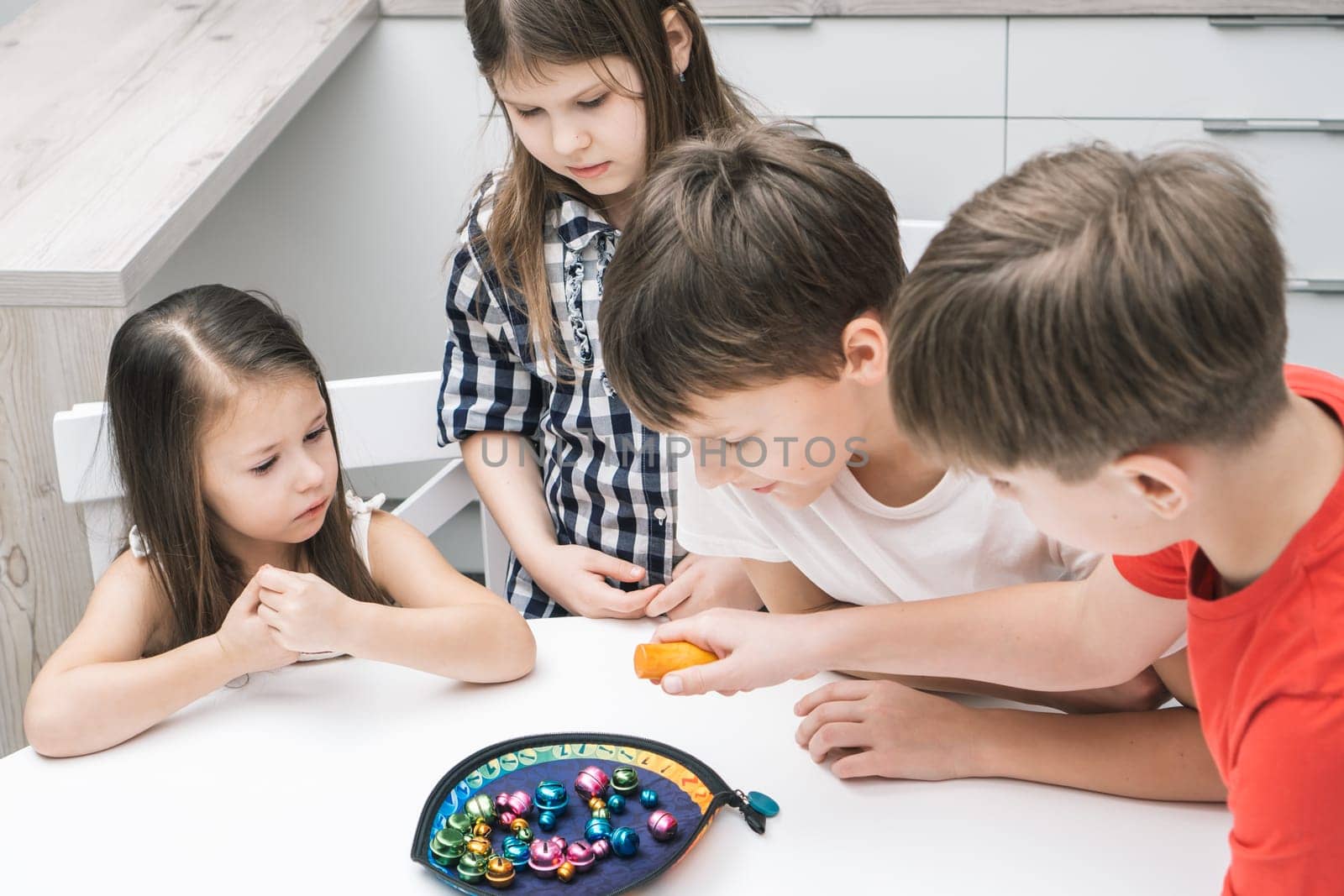 Group of friends play toy fishing on table. Hand of child hold fishing rod and pick up colorful metal playthings from plate. Home leisure, funny playtime. Entertaining interesting board game.