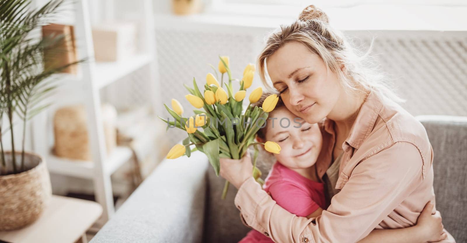 Mother and daughter sitting on the sofa and hugging. Concept of the mother's day, birthday and motherhood.