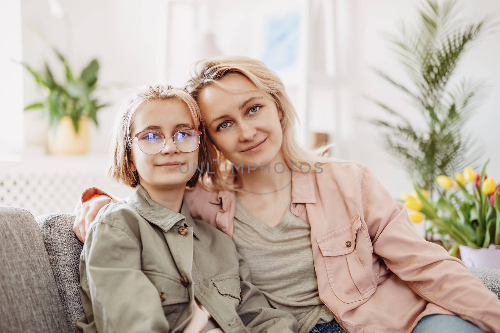 Mother and daughter sitting on the sofa indoor and embracing. Concept of the mother's day and motherhood.