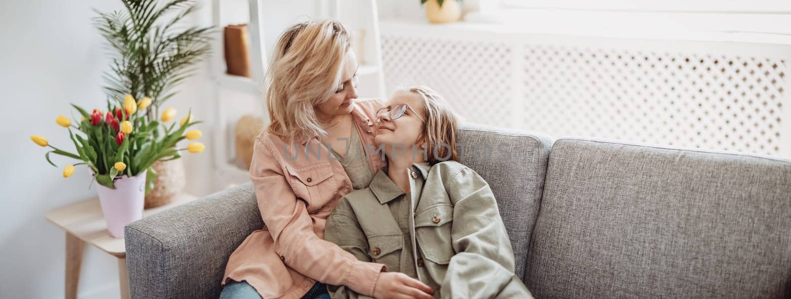 Mother and daughter sitting on the sofa indoor and embracing. Concept of the mother's day, birthday and motherhood.