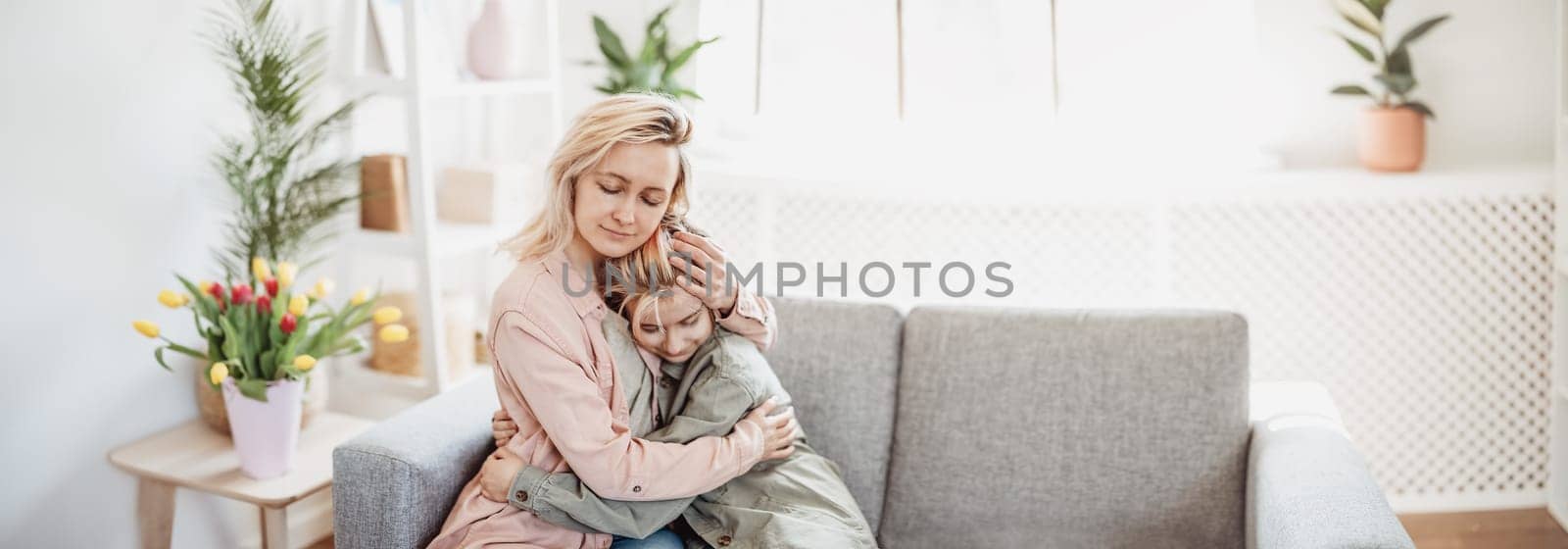 Mother and daughter sitting on the sofa indoor and embracing. Concept of the mother's day, birthday and motherhood.