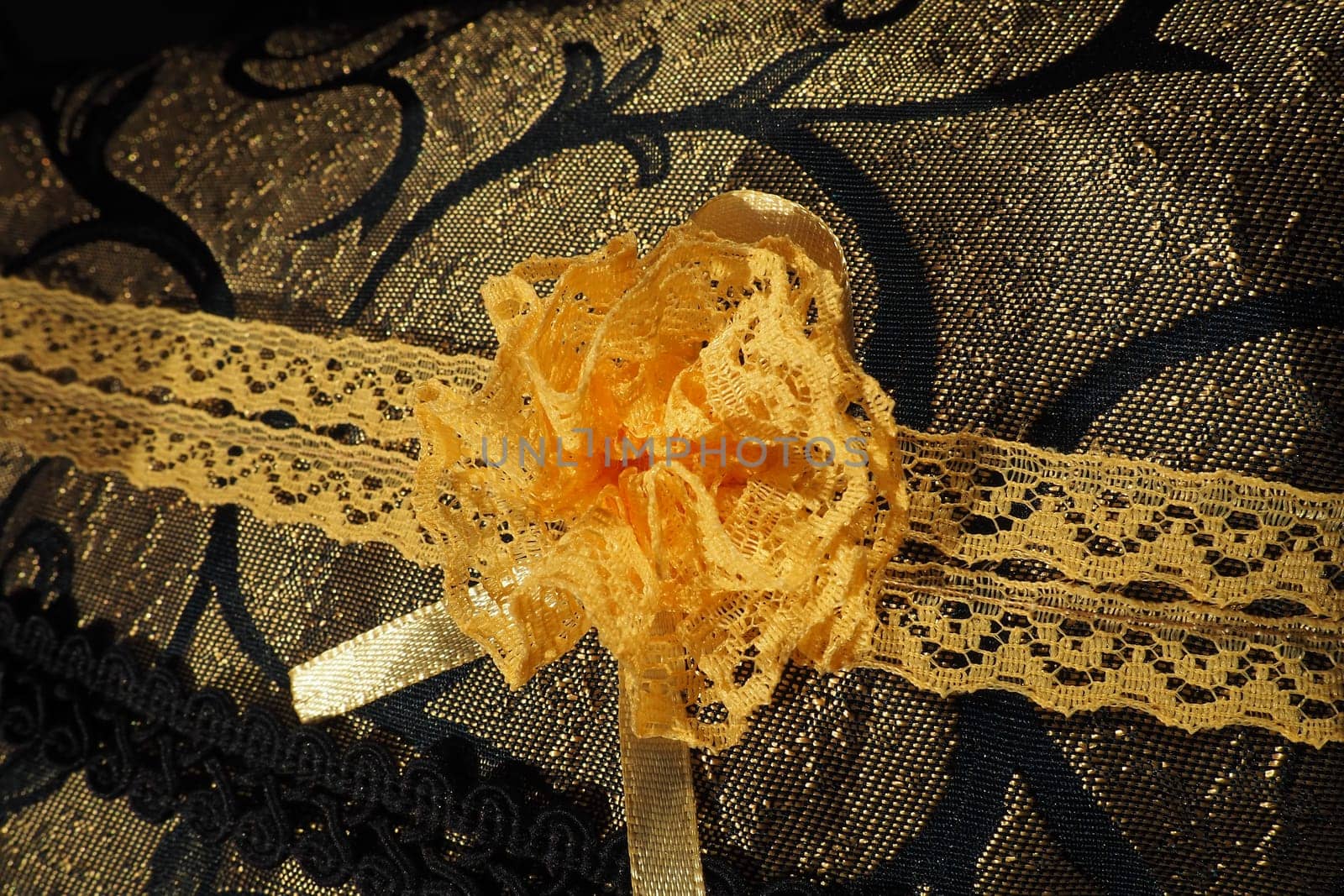 A beautiful yellow-orange lace artificial flower sewn onto a decorative cushion satin fabric. Blue dense braid with thin polyester lace. Decoration of decorative pillowcases. Women's needlework.