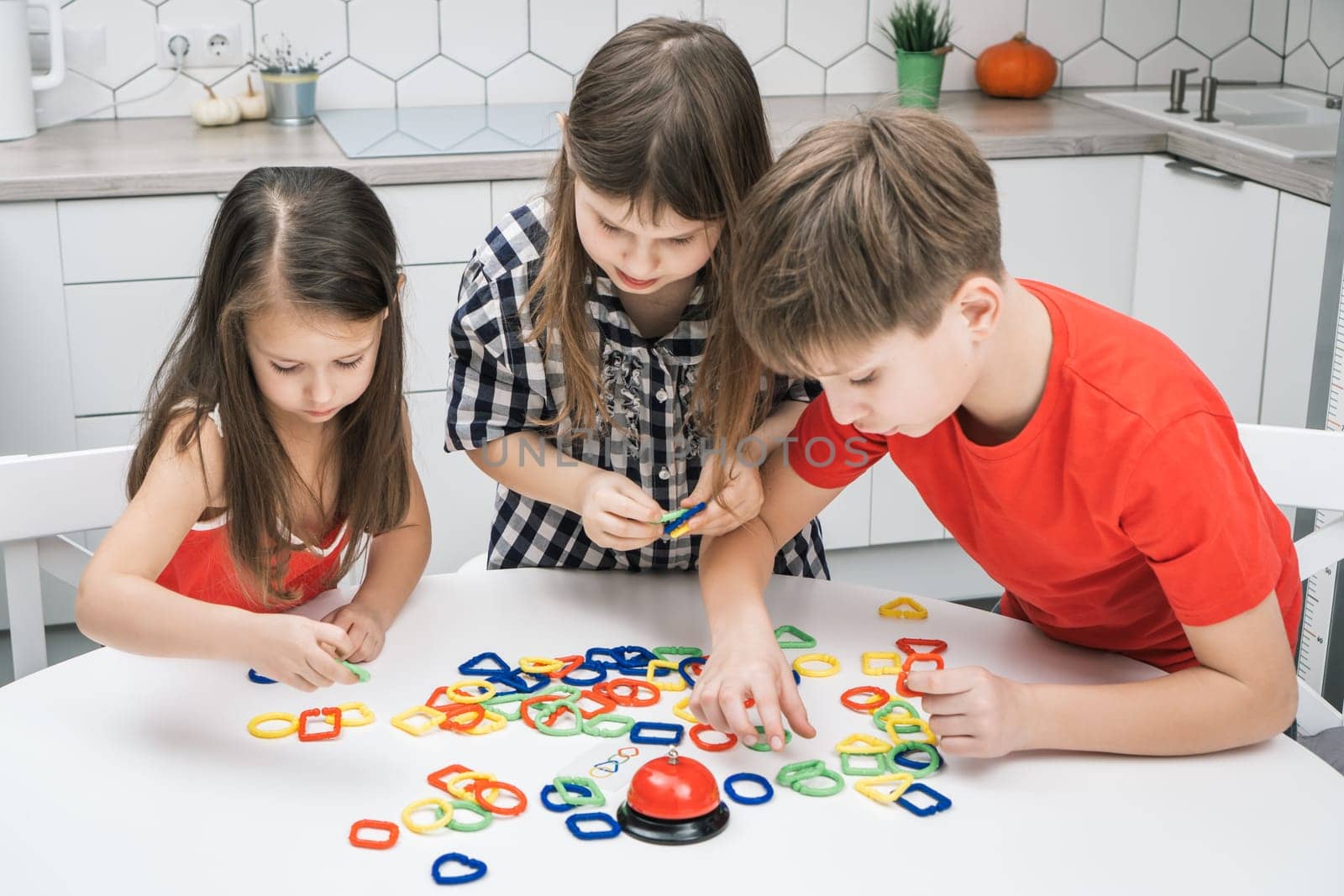 Funny school kids play toy constructor standing above kitchen table and looking down, from above view. Boy and girls collect plastic colored geometric figures. Entertaining interesting board game.