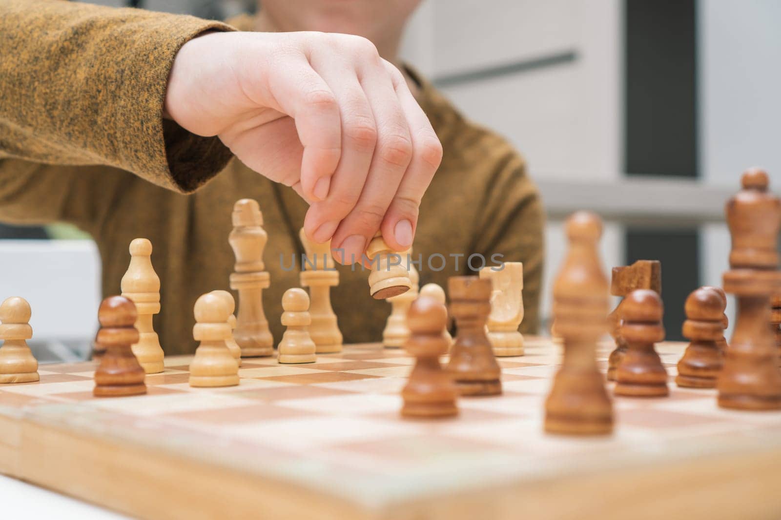 Boy play chess sitting at table closeup. Hand of child move white pawn on wooden chessboard. Game strategy, tactics. Home leisure, playtime, hobby. Educational interesting board game.