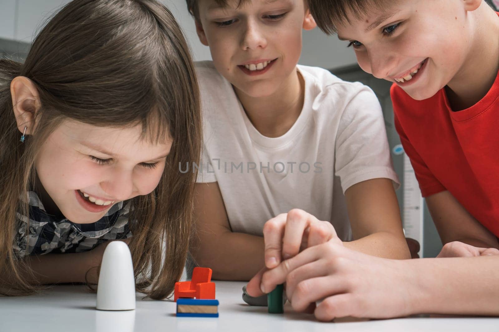 Joyful little school kids play toy mini furniture on table closeup. Portrait of children holding small plastic details. Home leisure, funny playtime. Entertaining interesting board game.