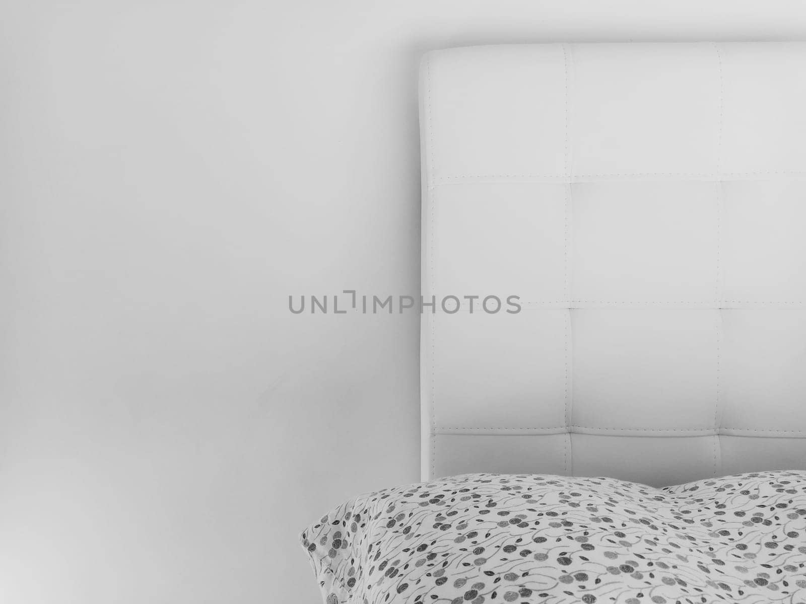 Soft headboard. Upholstery for furniture made of genuine or artificial leather and quilted fabric. Soft headboard against a light wall. Black and white monochrome photo.