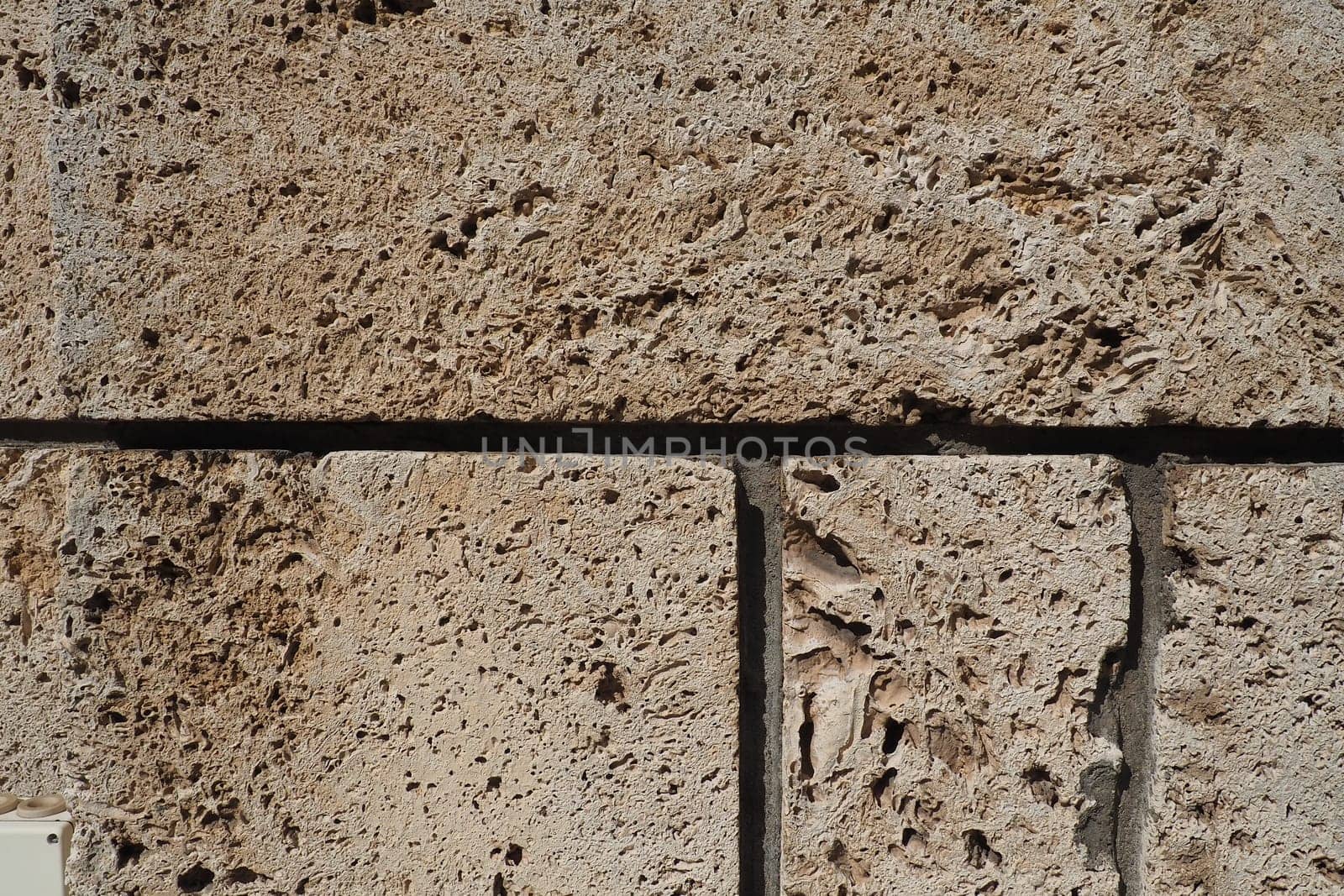 Textured wall lined with beige shell rock tiles. Close-up of a wall made of ancient shell rock. Holes, irregularities of natural building material. Church wall in Banja Koviljaca, Serbia.