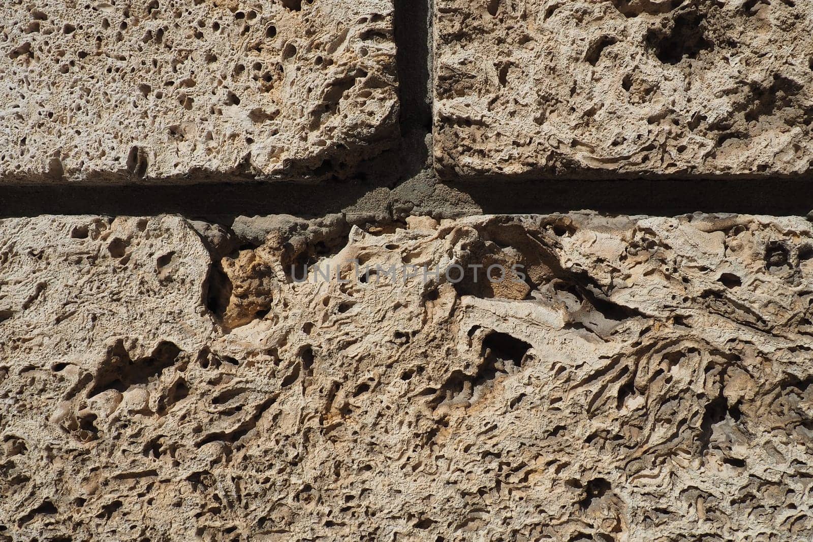 Textured wall lined with beige shell rock tiles. Close-up of a wall made of ancient shell rock. Holes, irregularities of natural building material. Church wall in Banja Koviljaca, Serbia.