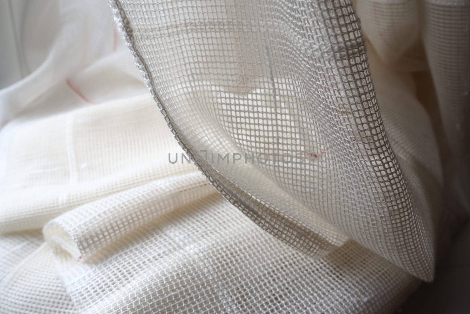 White coarse cotton or linen curtains made of weaves of thin threads. Simple compact economical apartment interior. Window decoration in the room. Red stripe. The fabric is folded in soft waves.