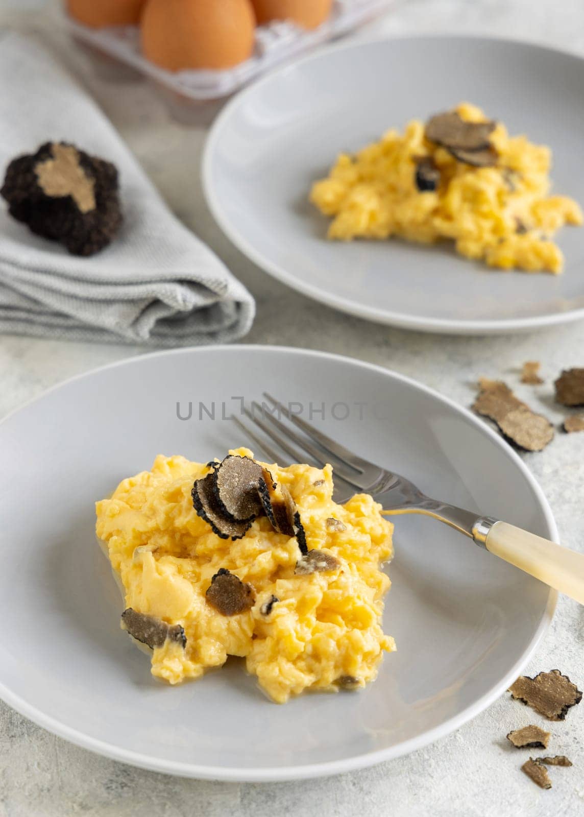 Scrambled eggs with sliced fresh black truffles from Italy served in a plate near fork and knife close up. Italian cousine, gourmet breakfast